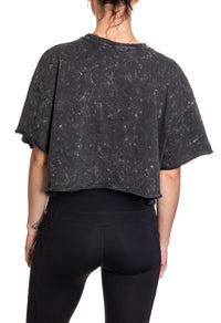 Load image into Gallery viewer, Woman turned around in front of a white background wearing an oversized, black, acid wash crop top - no designs present on the back of the shirt.
