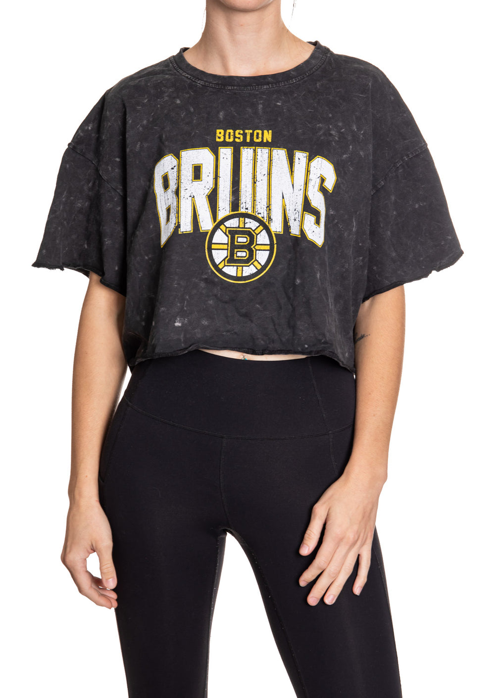 Woman standing in front of a white background wearing an oversized, black, acid wash crop top - featuring a Boston Bruins logo in the center of the shirt.