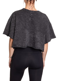 Load image into Gallery viewer, Woman turned around in front of a white background wearing an oversized, black, acid wash crop top - no designs present on the back of the shirt.
