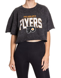 Load image into Gallery viewer, Woman standing in front of a white background wearing an oversized, black, acid wash crop top - featuring a Philadelphia Flyers logo in the center of the shirt.
