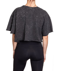 Load image into Gallery viewer, Woman turned around in front of a white background wearing an oversized, black, acid wash crop top - no designs present on the back of the shirt.
