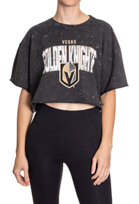 Load image into Gallery viewer, Woman standing in front of a white background wearing an oversized, black, acid wash crop top - featuring a Vegas Golden Knights logo in the center of the shirt.
