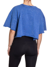 Load image into Gallery viewer, Woman turned around in front of a white background wearing an oversized, blue, acid wash crop top - no designs present on the back of the shirt.

