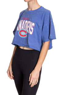 Load image into Gallery viewer, Woman standing sideways in front of a white background wearing an oversized, blue, acid wash crop top - featuring a Montreal Canadians logo in the center of the shirt.
