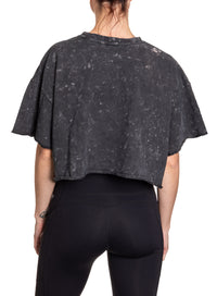 Load image into Gallery viewer, Woman turned around in front of a white background wearing an oversized, black, acid wash crop top - no designs present on the back of the shirt.
