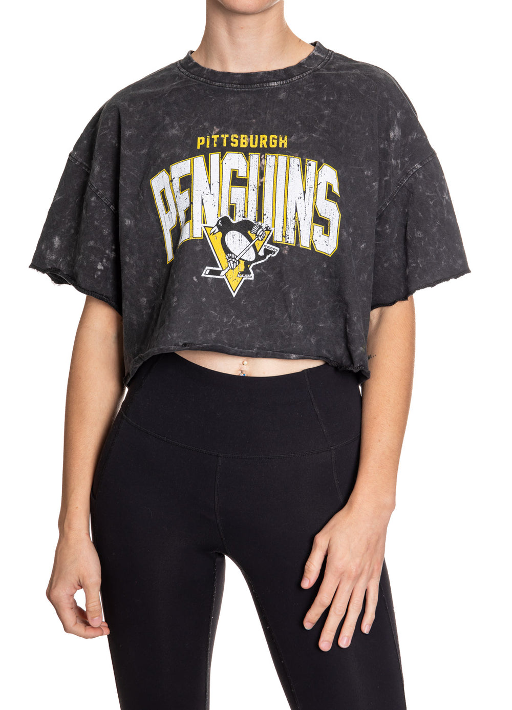 Woman standing in front of a white background wearing an oversized, black, acid wash crop top - featuring a Pittsburgh Penguins logo in the center of the shirt.