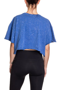 Load image into Gallery viewer, Woman turned around in front of a white background wearing an oversized, blue, acid wash crop top - no designs present on the back of the shirt.
