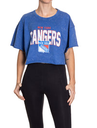 Load image into Gallery viewer, Woman standing in front of a white background wearing an oversized, blue, acid wash crop top - featuring a New York Rangers logo in the center of the shirt.
