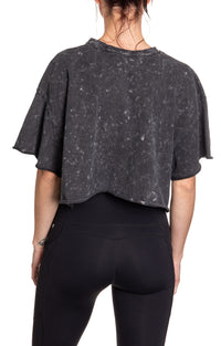 Load image into Gallery viewer, Woman turned around in front of a white background wearing an oversized, black, acid wash crop top - no designs present on the back of the shirt.

