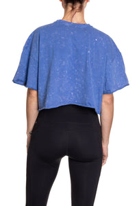 Load image into Gallery viewer, Woman turned around in front of a white background wearing an oversized, blue, acid wash crop top - no designs present on the back of the shirt.
