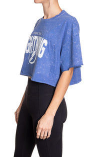 Load image into Gallery viewer, Woman standing sideways in front of a white background wearing an oversized, blue, acid wash crop top - featuring a Tampa Bay Lightning logo in the center of the shirt.
