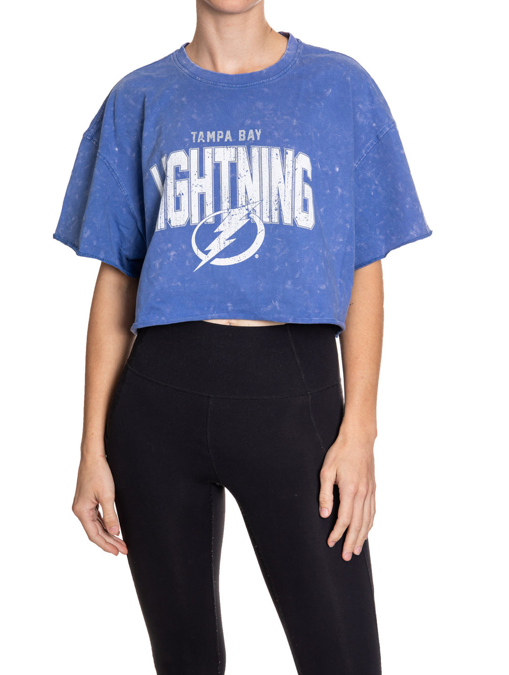 Woman standing in front of a white background wearing an oversized, blue, acid wash crop top - featuring a Tampa Bay Lightning logo in the center of the shirt.
