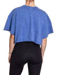 Load image into Gallery viewer, Woman turned around in front of a white background wearing an oversized, blue, acid wash crop top - no designs present on the back of the shirt.
