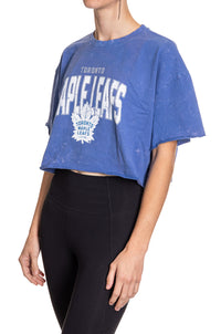 Load image into Gallery viewer, Woman standing sideways in front of a white background wearing an oversized, blue, acid wash crop top - featuring a Toronto Maple Leafs logo in the center of the shirt.
