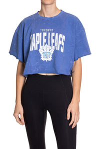 Load image into Gallery viewer, Woman standing in front of a white background wearing an oversized, blue, acid wash crop top - featuring a Toronto Maple Leafs logo in the center of the shirt.
